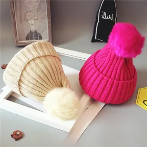 Détail de la maille côtelée et des pompons en fausse fourrure sur les bonnets bébé