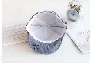 Detailansicht der Baby-Sonnenmütze aus grauem Denim mit gesticktem Lächeln am Schirm