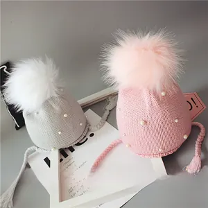 Détail de bonnets tricotés pour bébé rose et gris avec perles et grands pompons