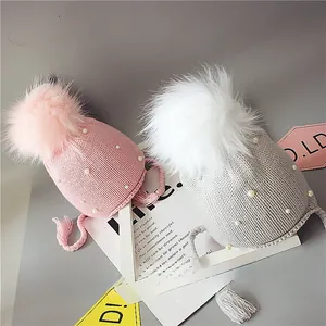 Vue détaillée des bonnets tricotés pour bébé rose et gris avec pompons et perles