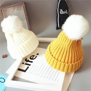 Détail de bonnets tricotés pour bébé en beige et jaune avec pompons en fausse fourrure