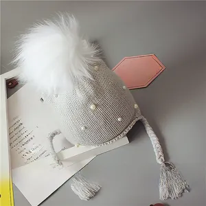 Détail d'un bonnet en tricot gris clair pour bébé avec pompons en fourrure et perles
