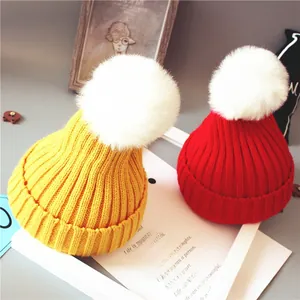 Gros plan détaillé de bonnets tricotés pour bébé en rouge et jaune avec pompons en fausse fourrure