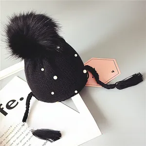 Détail du bonnet en tricot noir pour bébé avec perles blanches et grand pompon en fourrure