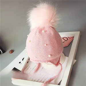 Détail du bonnet en tricot rose pour bébé avec pompon en fourrure et perles blanches
