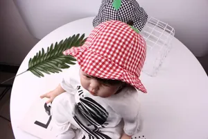 Detail shot of red checkered baby bucket hat with green leaf accent on a white table