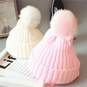 Détail de bonnets tricotés pour bébé avec texture côtelée et grands pompons en fourrure