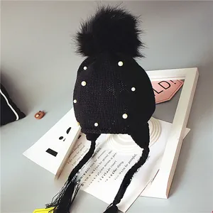 Détail du bonnet en maille noir avec pompon en fausse fourrure et perles blanches