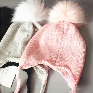 Détail de bonnets tricotés pour bébé avec pompons et perles en rose, gris et noir