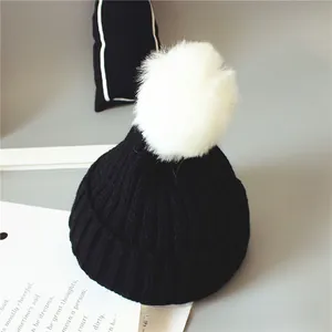 Détail d'un bonnet en maille côtelée noire avec un pompon en fausse fourrure blanche