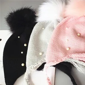 Trois bonnets tricotés pour bébé avec gros pompons, perles et attaches en noir, gris et rose