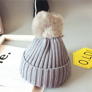 Détail du bonnet tricoté gris pour bébé avec pompon en fausse fourrure beige doux