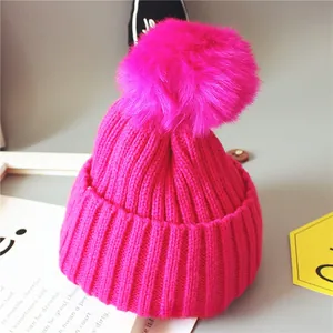 Détail du bonnet en tricot fuchsia pour bébé avec un grand pompon en fausse fourrure