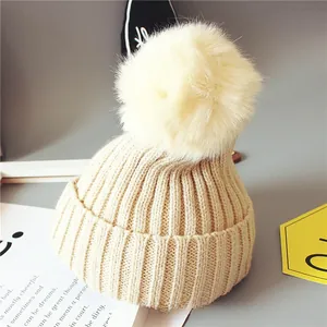 Détail de la maille côtelée épaisse du bonnet bébé beige avec un grand pompon en fourrure