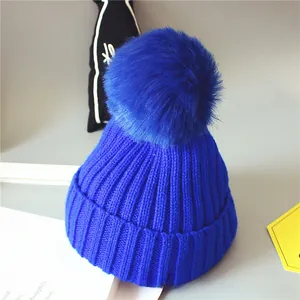 Détail d'un bonnet en maille côtelée bleu roi avec un grand pompon en fourrure synthétique
