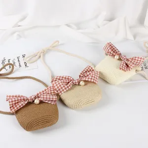Three colors of children's straw bags featuring a bow and pearl decoration on white fabric