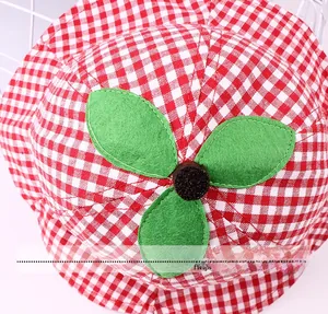 Top view detail of a red and white plaid baby sun hat with green felt leaf decorations