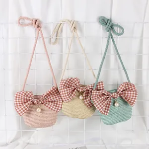 Three children's straw bags in pink, green, and beige with bows and pearl charms