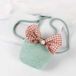 Detail of green straw mini crossbody bag with a large plaid bow and pearl accent
