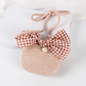 Detail of straw woven kids bag with a plaid bow, large pearl, and pink rope strap