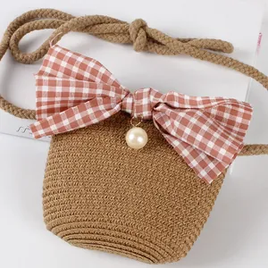 Detail of hand-woven straw crossbody bag with pink plaid bow and pearl charm