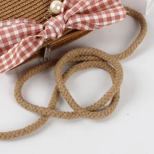 Detail of straw woven bag with pink plaid bow, pearl pendant and thick cotton rope strap