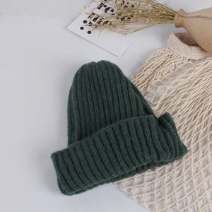 Detailed close-up of dark green rib-knit beanie hat featuring a thick folded cuff