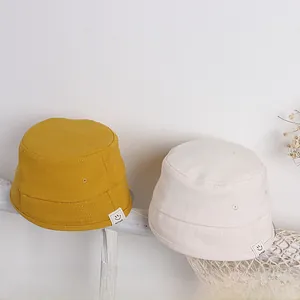 Detail von gelben und beige Segeltuch-Fischerhüten mit Smiley-Etikett im Regal