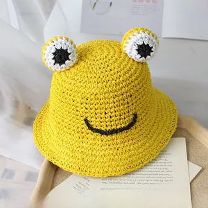 Détail d'un chapeau de paille jaune tissé main avec yeux de grenouille et visage souriant