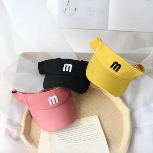 Close-up of three sun visors with embroidered 'm' in pink, yellow, and black on a tray