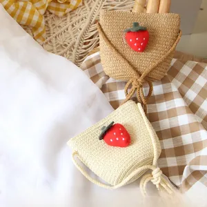 Detail view of woven straw shoulder bags for kids with red strawberry decorations
