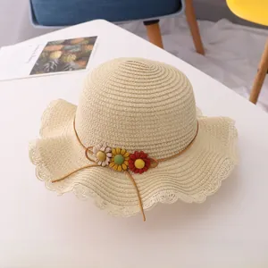 Detail of light beige straw sun hat with wavy brim and three colorful daisy flowers