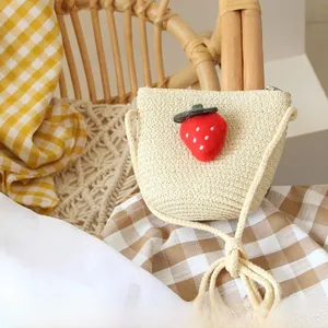 Detail of hand-woven straw bag for kids featuring a red plush strawberry and cotton rope strap