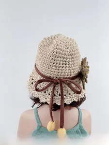 Détail d'un chapeau en paille avec un ruban marron et une décoration florale olive