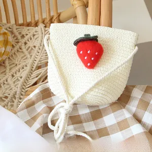Detail of woven straw texture and plush strawberry charm on cream kids crossbody bag
