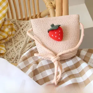 Detail of handmade straw crossbody bag for kids featuring a red strawberry decorative charm
