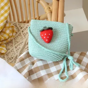 Detail of mint green straw woven children's crossbody bag with 3D plush strawberry charm