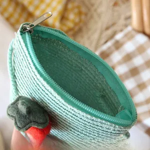 Detail of mint green woven crossbody bag featuring a strawberry charm and zipper closure