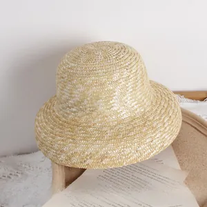 Détail du tissage d'un chapeau de paille naturel pour filles sur plateau en céramique beige