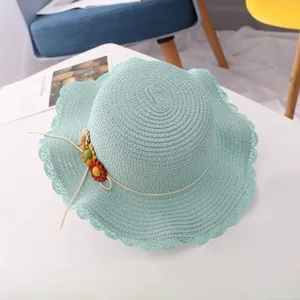 Detail of light blue straw sun hat featuring wavy edges and decorative fabric flowers