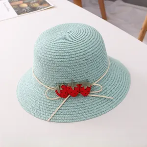 Détail d'un chapeau de paille vert menthe orné de trois petites fraises en tissu rouge