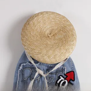 Close-up of children's straw beret featuring white lace ribbons and woven texture