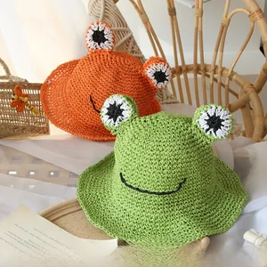 Detail of hand-woven kids straw hats featuring cute cartoon frog designs in orange and green