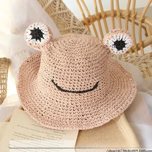 Detailed texture of pink hand-woven straw hat for kids featuring cute frog face design