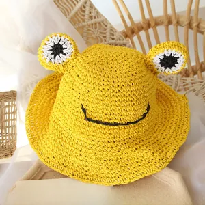 Detail of hand-woven straw kids hat featuring cartoon frog eyes and smile design
