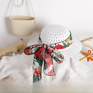 Detail of white woven straw hat with colorful floral ribbon bow on lace background