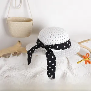 White hollow-woven sun hat for kids with a black polka dot ribbon and matching straw bag