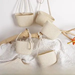 Detailed close-up of five handmade mini woven straw bags hanging on rustic wooden branches