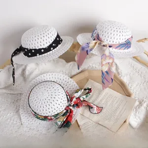 Close-up of children's white straw hats with floral ribbon bows on a lace background