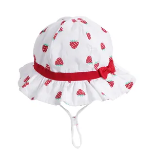 White cotton baby sun hat with strawberry print, red bow, and adjustable chin strap